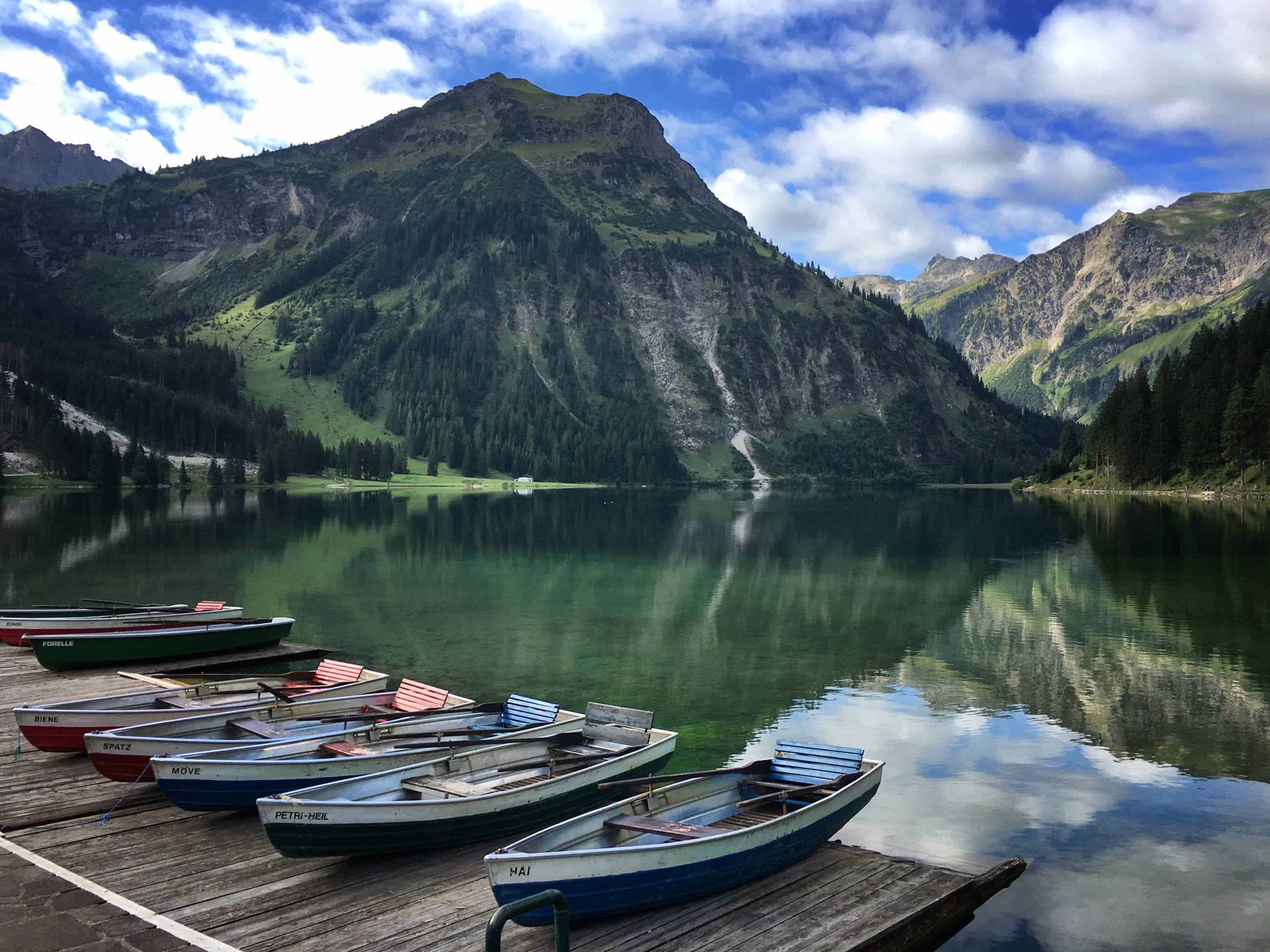 Rowing boats moored on a still alpine lake below steep green mountains