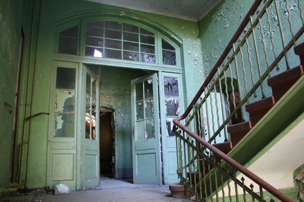 A green-painted stairwell and double doors in an abandoned building