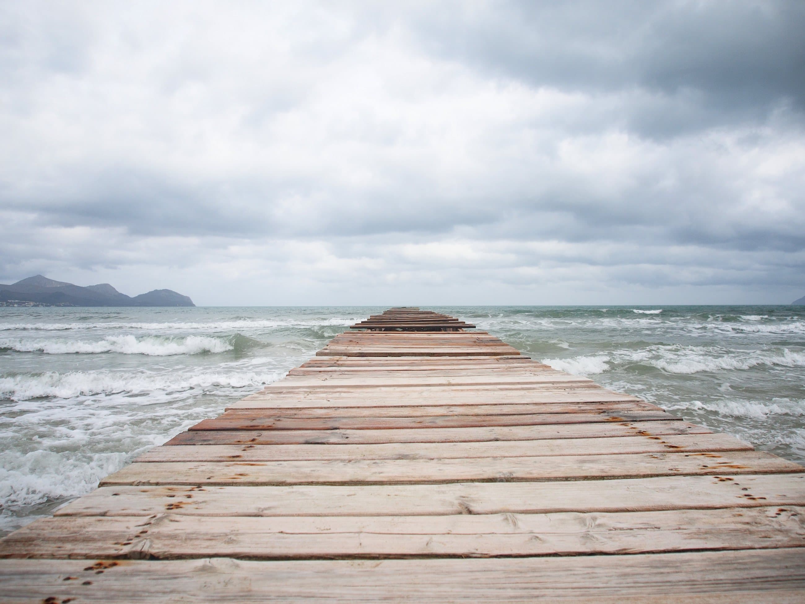 A weathered wooden jetty running out into a grey, choppy sea under heavy cloud