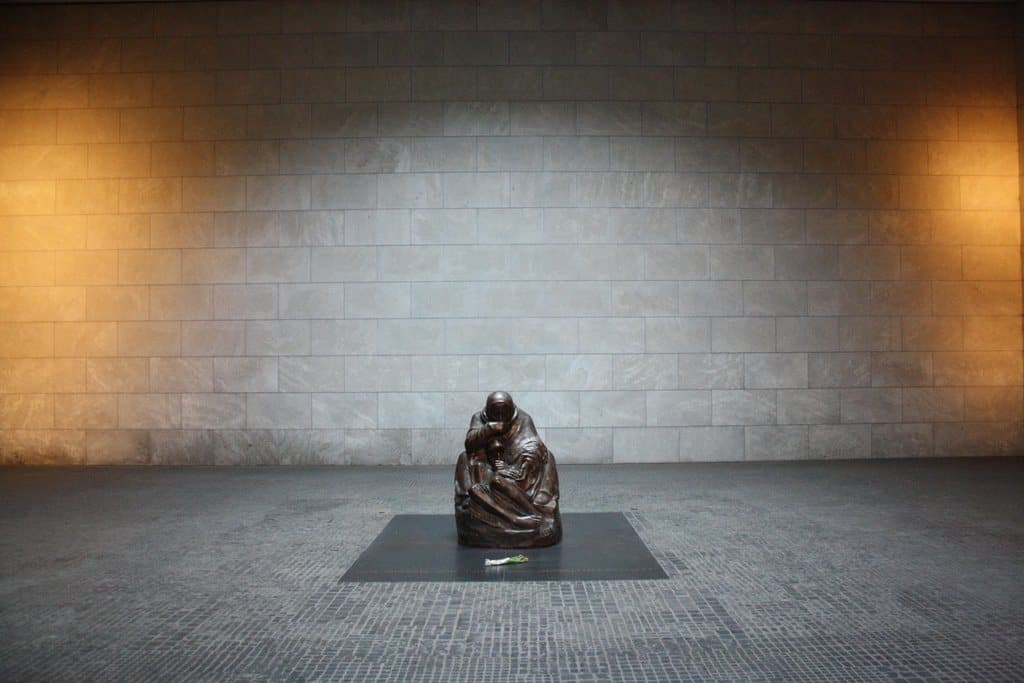 A bronze sculpture alone in a bare stone hall under a skylight