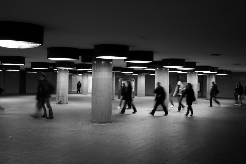 People crossing a low underground hall of columns, in black and white