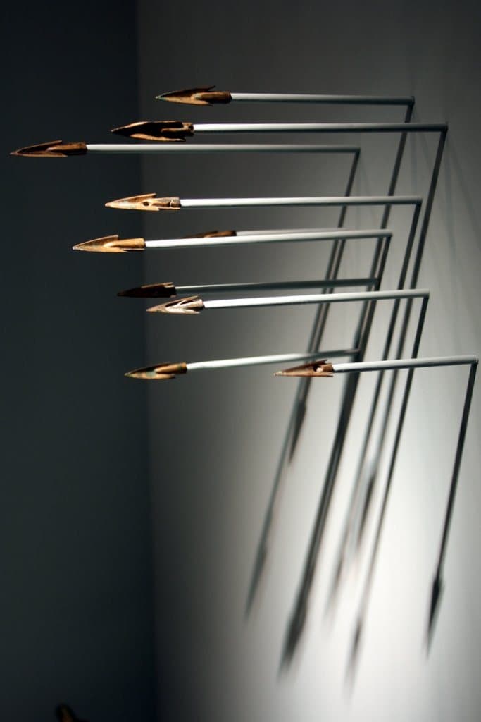 Metal arrows mounted on a white wall casting long shadows